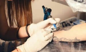 tatuatrice che effettua un tattoo sul braccio di un cliente
